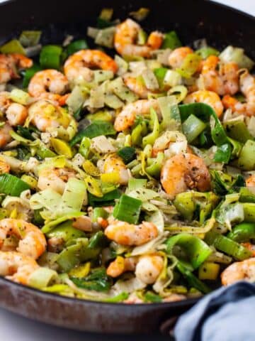 A closeup of a large skillet filled with sauteed shrimp and leeks.