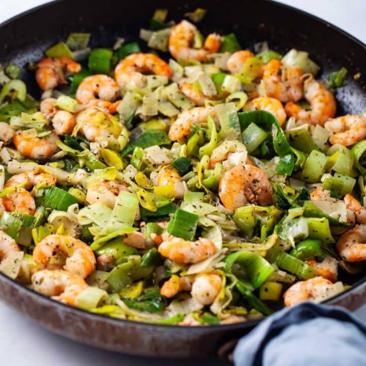 A closeup of a large skillet filled with sauteed shrimp and leeks.