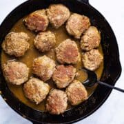 A spoon resting in a cast iron skillet with curried bison meatballs.