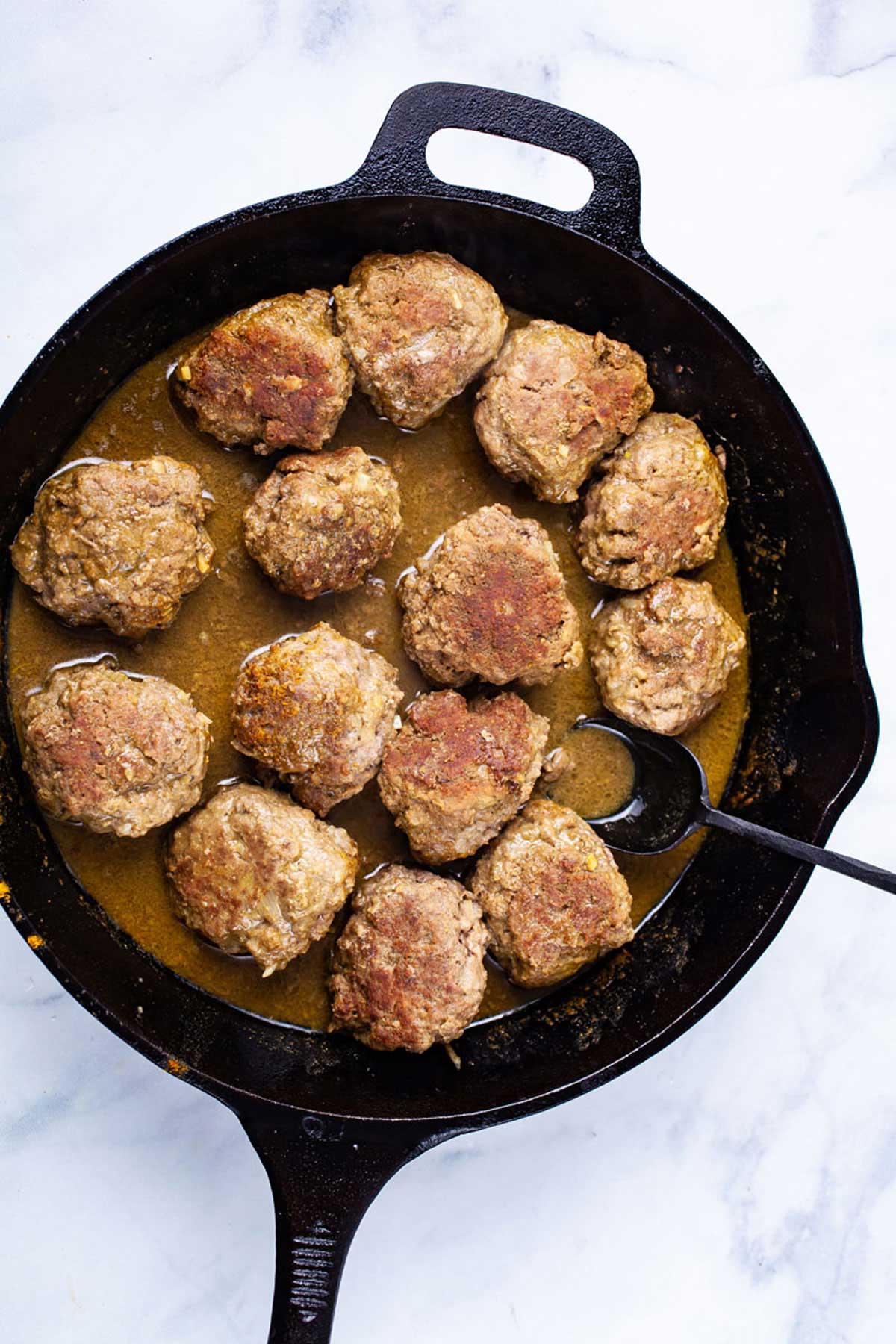 A spoon resting in a cast iron skillet with curried bison meatballs.