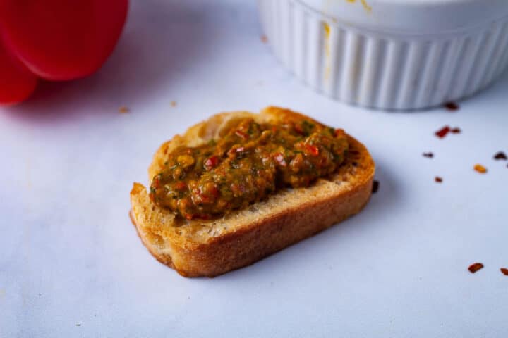 A close up of a roasted crostini bread topped with a dark reddish spread.