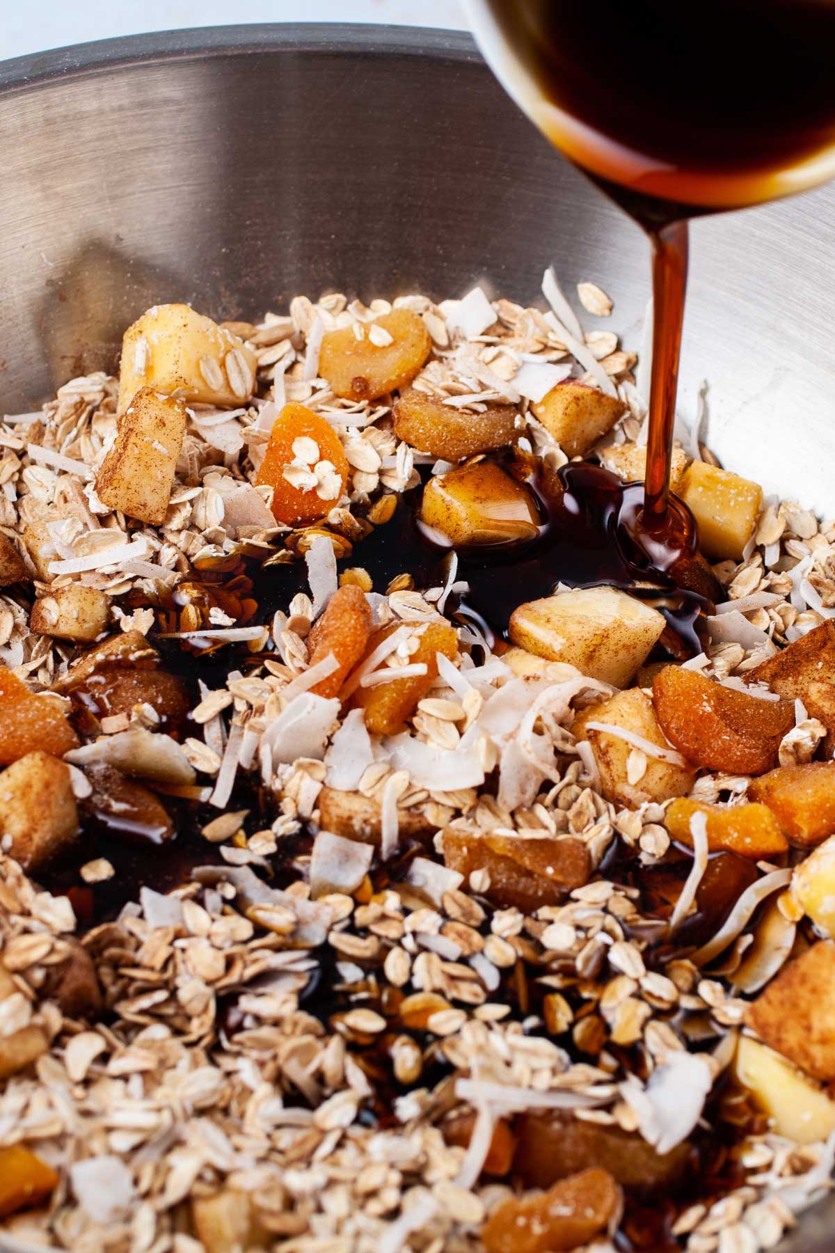 Maple syrup poured over an oat mixture in a large mixing bowl.