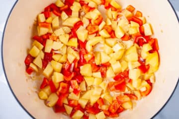 Chopped potatoes, onions, and red bel pepper in a Dutch pan.