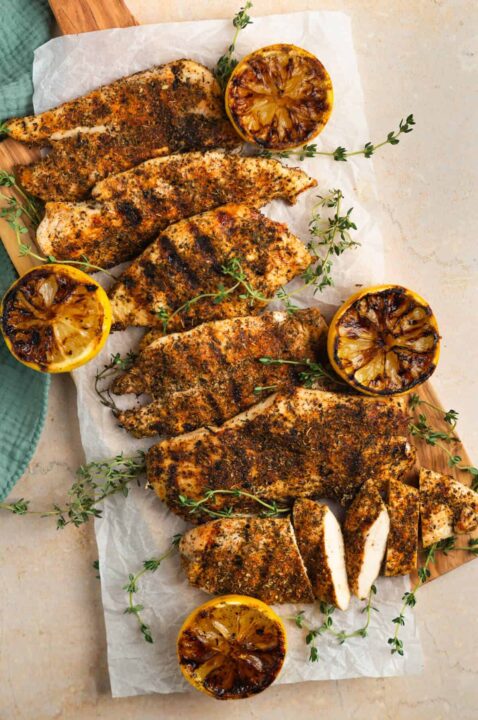 an overhead shot of herb crusted chicken breasts on a piece of parchment paper surrounded by thyme sprigs and charred lemon.