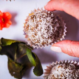 A hand grabbing an energy ball sprinkled with dried coconut flakes and served in tiny paper cupcake holder.