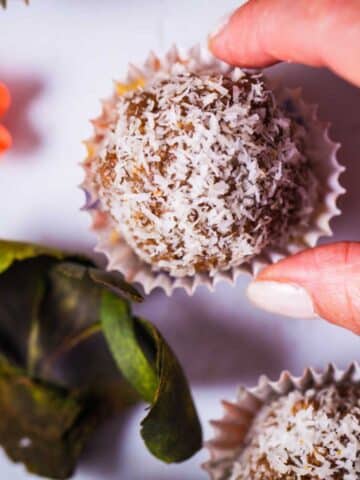 A hand grabbing an energy ball sprinkled with dried coconut flakes and served in tiny paper cupcake holder.
