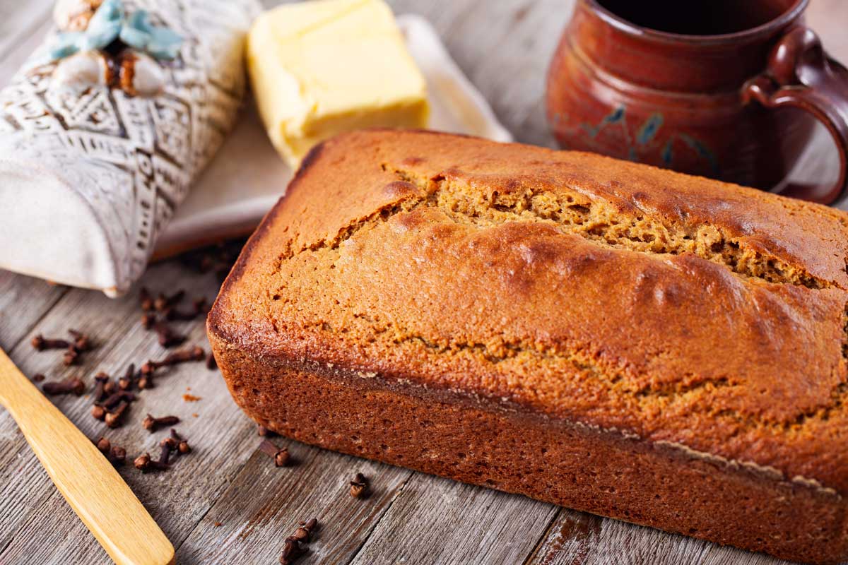 A loaf of orange bread displayed next to a butter cup holder and tea cup.