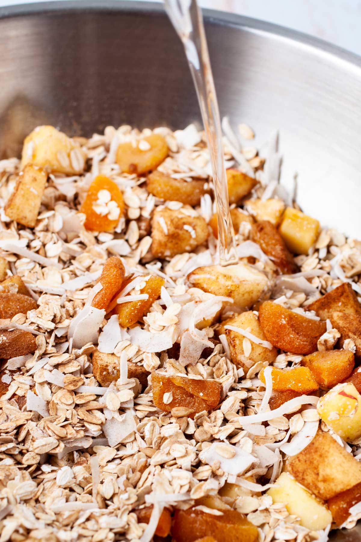 Coconut oil poured over an oat mixture in a large mixing bowl.