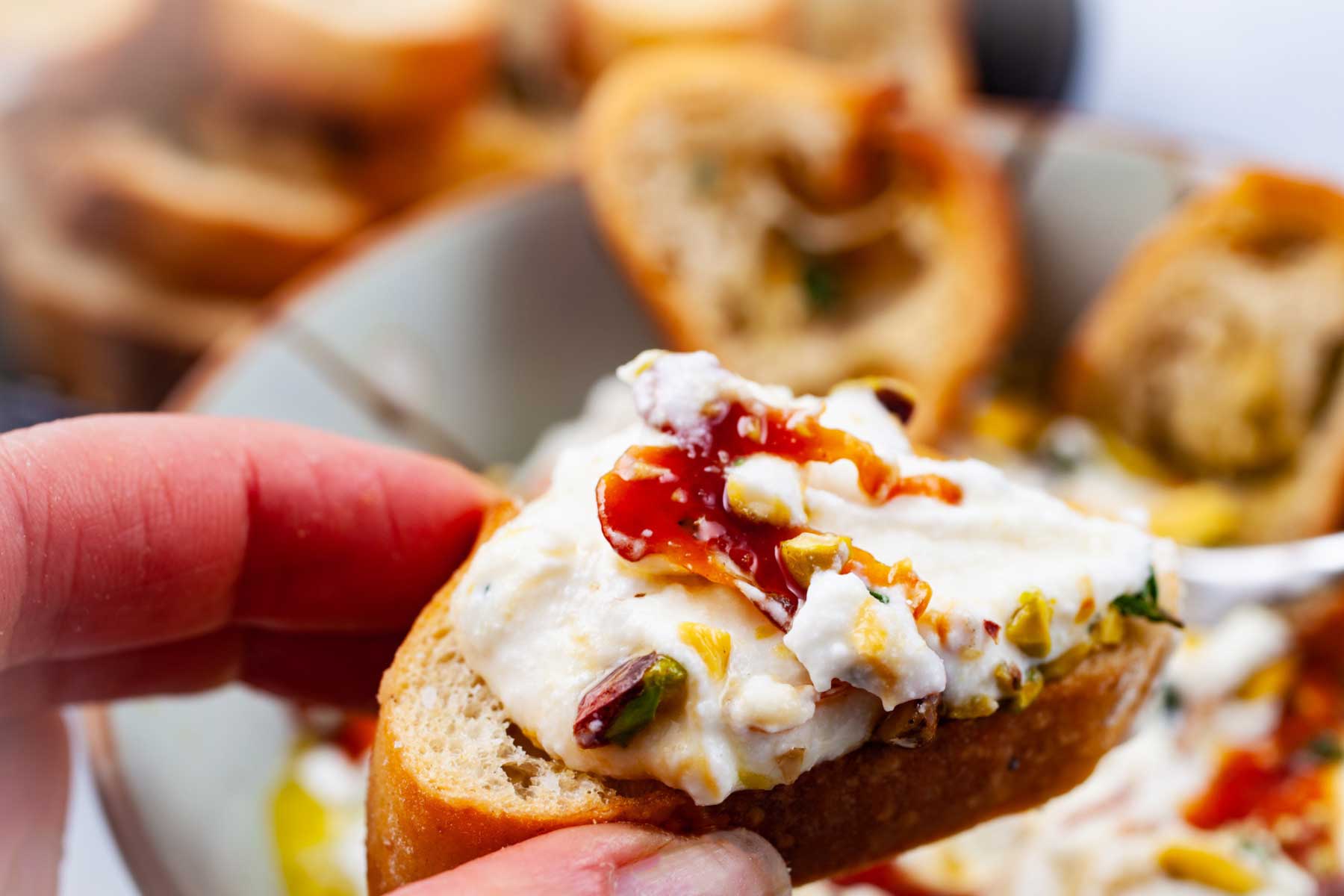 A hand holding crostini topped with whipped ricotta and honey.