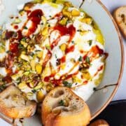 Whipped ricotta with honey in a bowl, topped with pistachios and served with crostini.