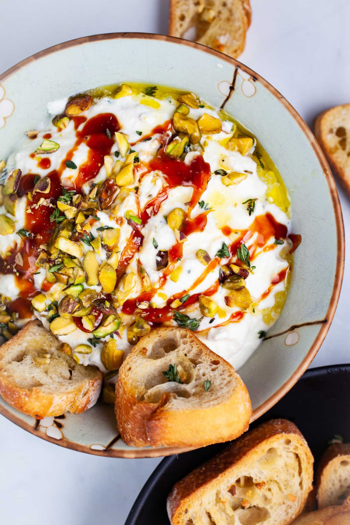 Whipped ricotta with honey in a bowl, topped with pistachios and served with crostini.