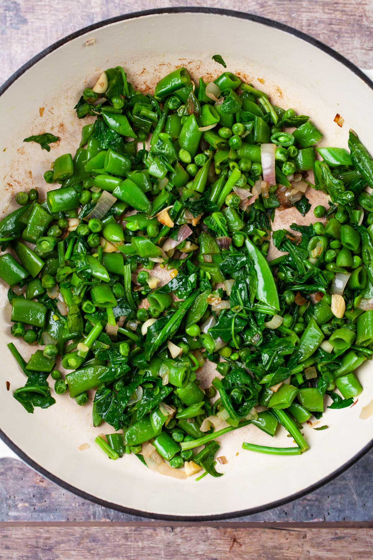 Peas, onions, garlic, and spinach sauteed in olive oil in a pan.