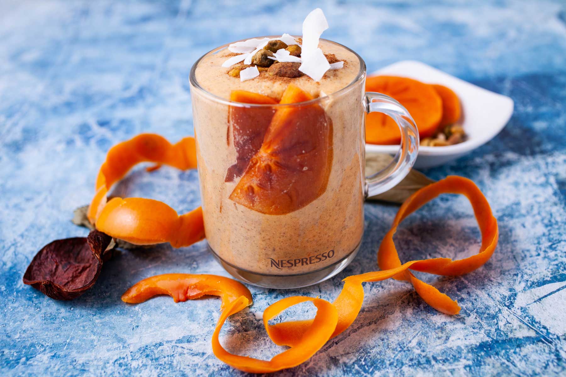 A creamy smoothie filled with persimmon slices and topped with nuts, shredded coconut and cinnamon.