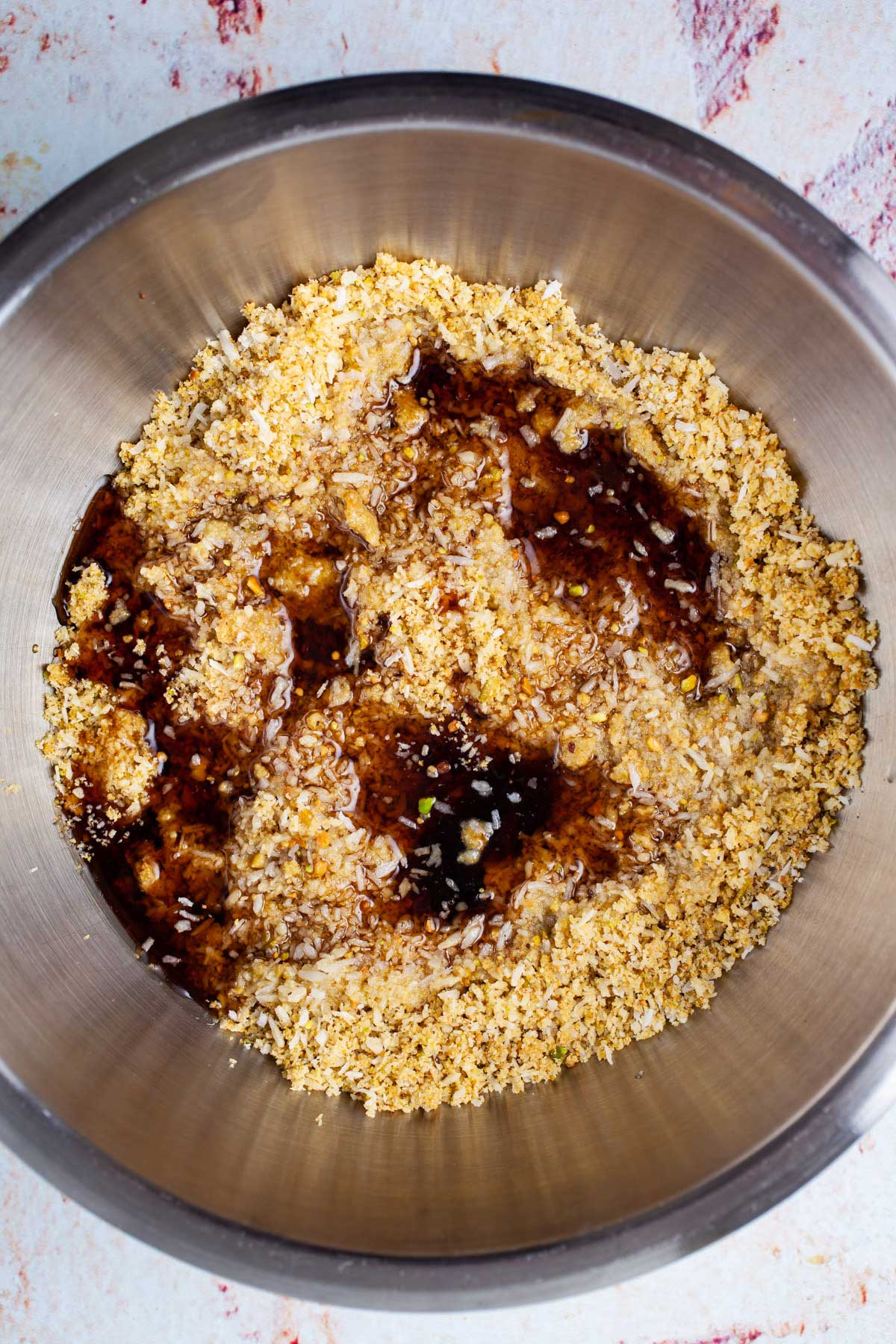 Maple syrup poured over a coconut meal in a stainless steel bowl.