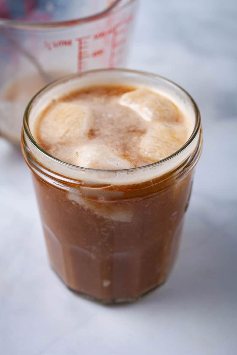 A mason jar with ice cubes and cashew milk infused cold brew coffee.