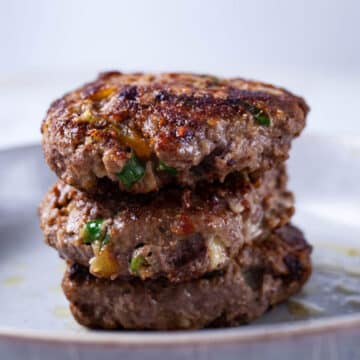 Three juicy cooked burgers stacked on top of each other on a plate.