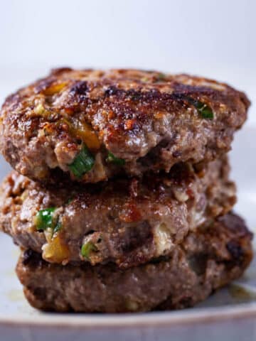 Three juicy cooked burgers stacked on top of each other on a plate.