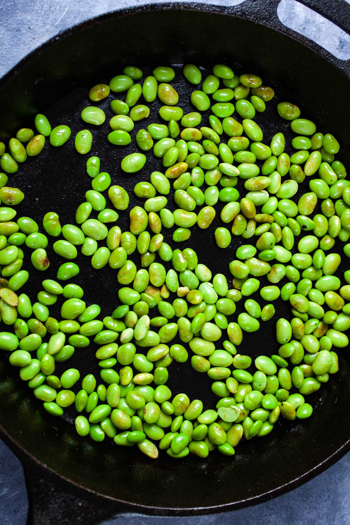 Fried edamame beans in a cast-iron pan.