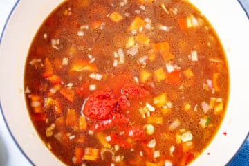 Red tomato paste added to chopped vegetables and broth in a Dutch pan.
