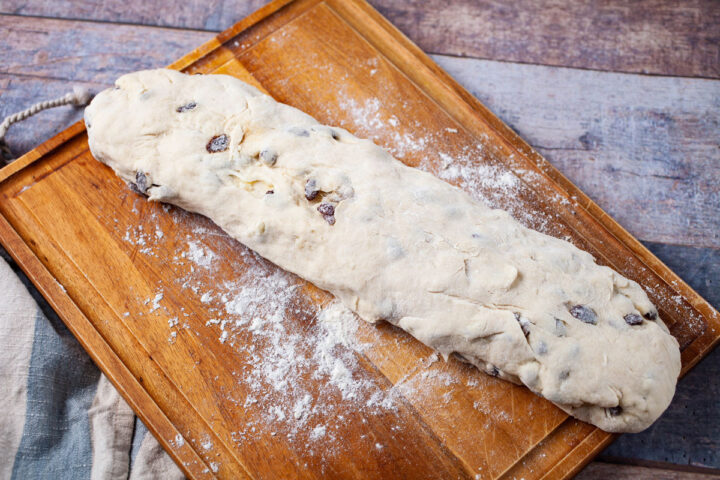 Raisins filled dough shaped like a baguette resting on a wooden board.