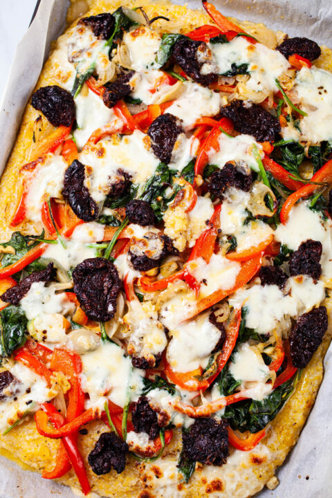 A family-style vegetable polenta pizza topped with spinach, red bell pepper, sun dried tomatoes, onions, garlic, and mozzarella cheese.