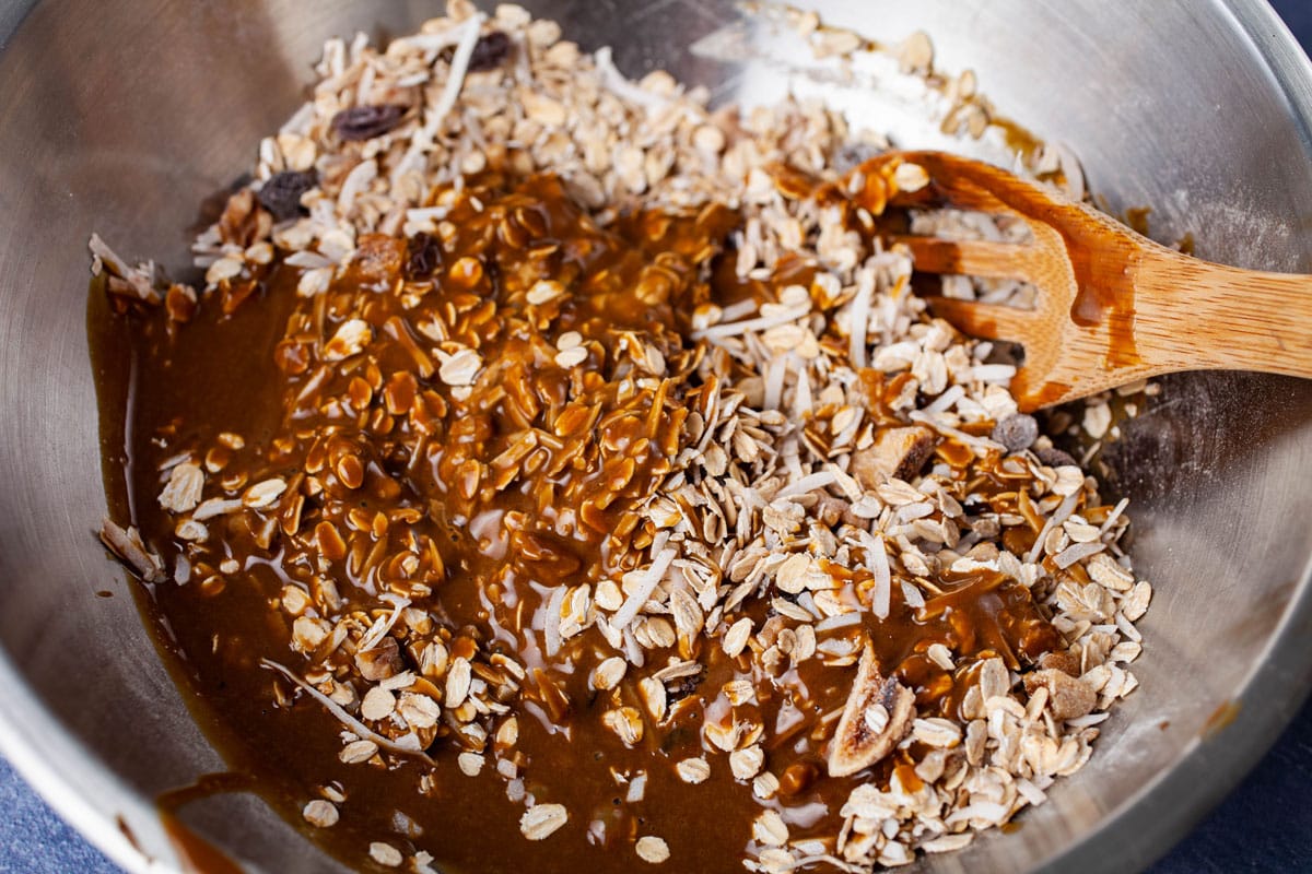 Dry oats mixed with a mixture of wet ingredients in a stainless steel bow in preparation for baking cookies.