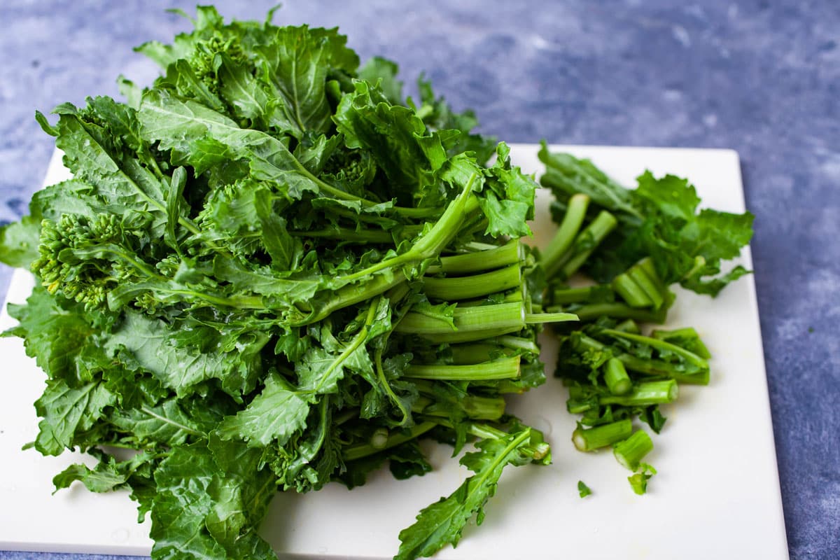 A bushel of broccoli rabe on a cutting board with ends cut off.