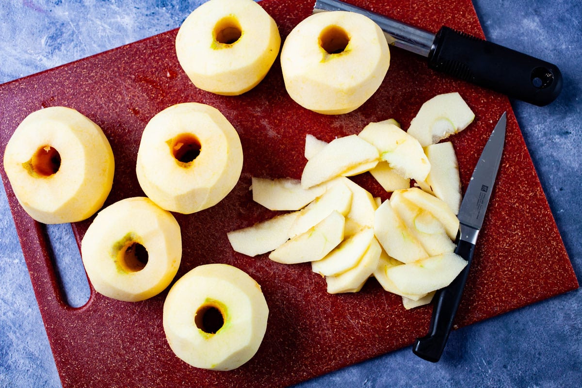 Cored and peeled apples on a cutting board next to one thinly sliced apple.