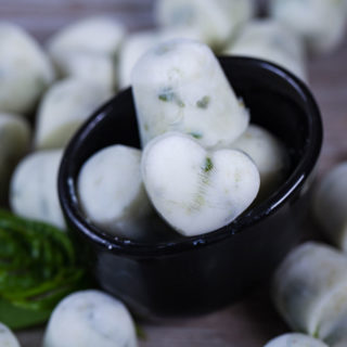 A close up of white ice cubes in a small bowl and surrounded by randomly placed ice cubes on a wooden board.