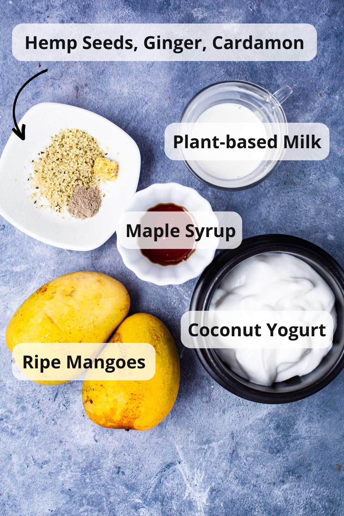 Ingredients like mangoes, maple syrup, ginger, hemp seeds, cardamom, yogurt displayed on a table.