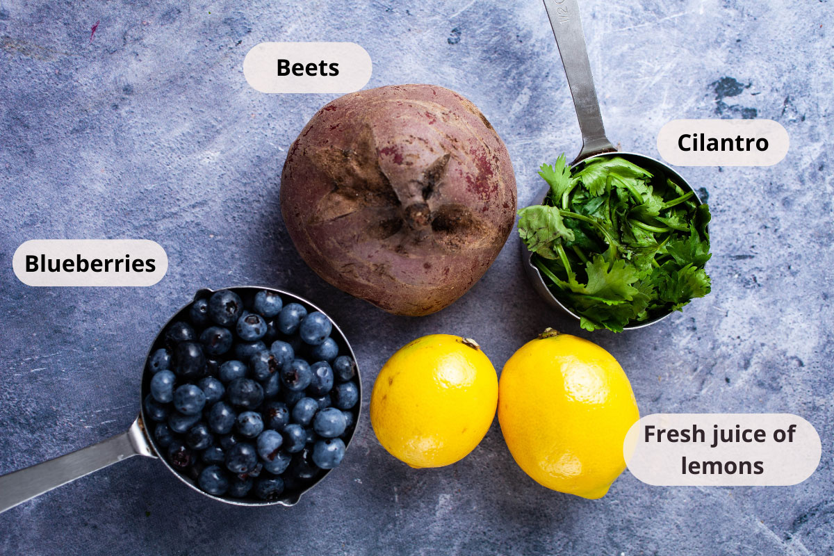 A large red beet, blueberries, cilantro, and two lemons displayed on a table.