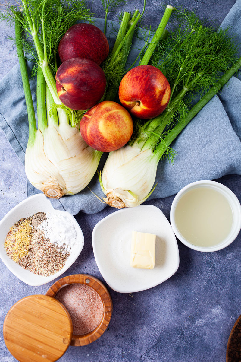 A table displaying fresh fennel bulbs, fresh whole peaches, butter, stock, salt, and other spices.