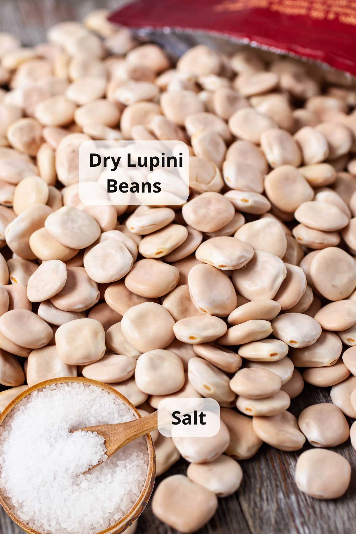 Dry lupini beans scattered on a wooden board next to a pot of salt.