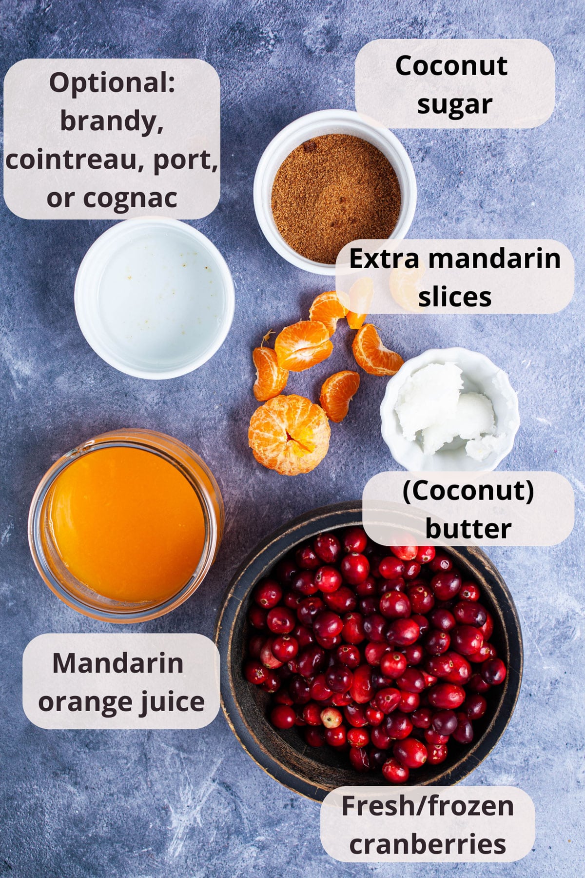 Brandy, coconut sugar, mandarin slices, coconut butter, mandarin orange juice, and fresh cranberries displayed on a table.