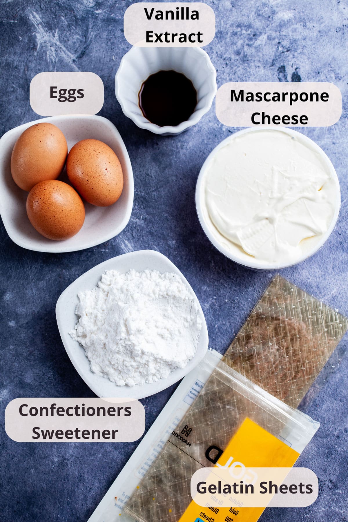 Gelatin sheets, mascarpone cheese, powdered sugar, three eggs, and vanilla extract displayed on a table.