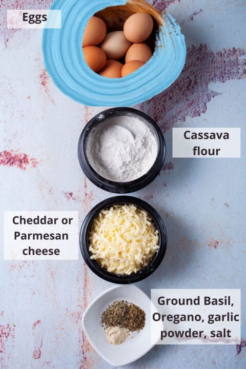 Ingredients like eggs, Cassava flour, cheese, and spices displayed on a table.