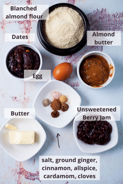 Blanched almond flour, almond butter, dates, egg, butter, warm spices, and berry jam displayed on a table.