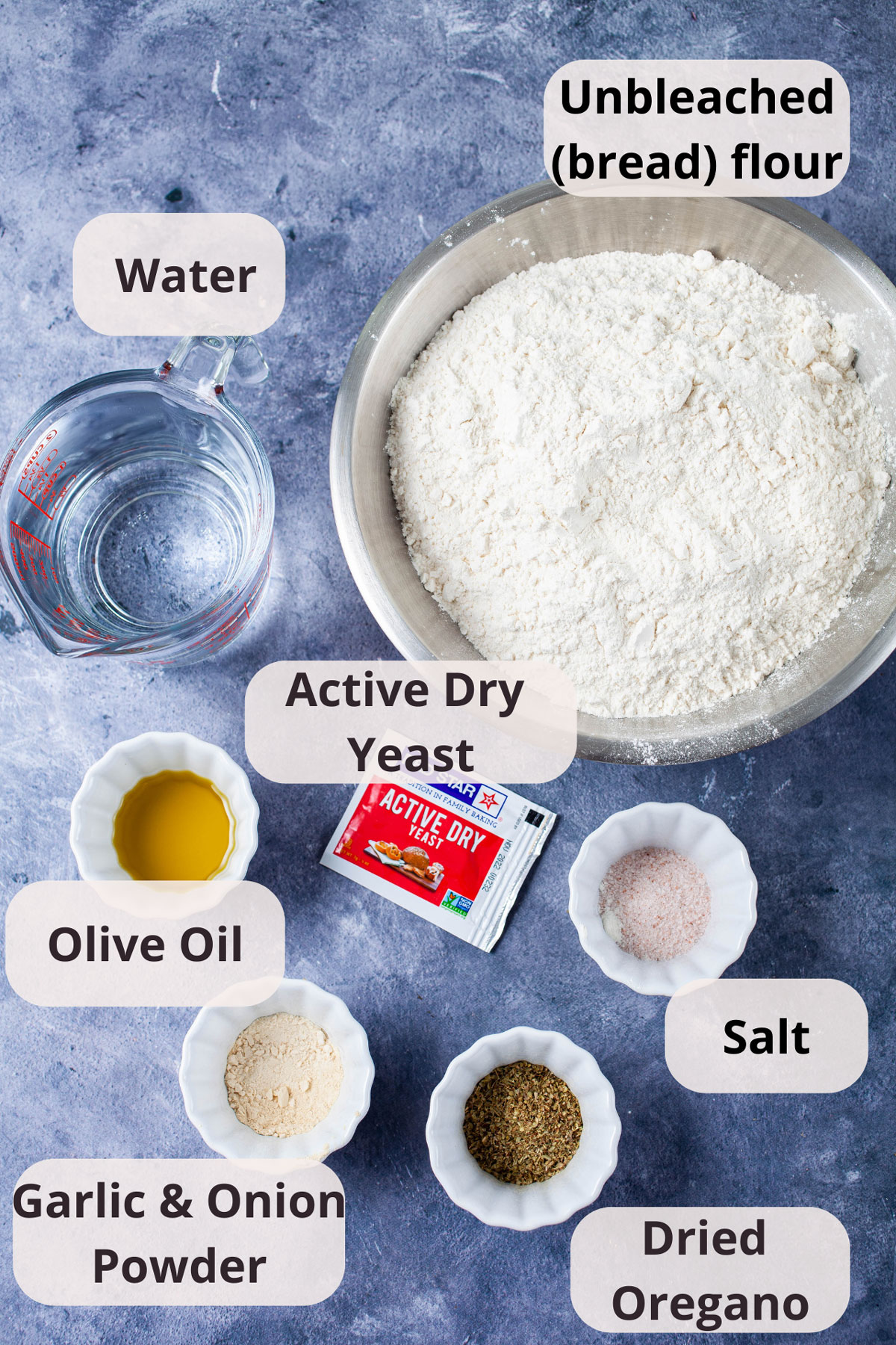 Unbleached flour, water, active dry yeast, olive oil, salt, garlic powder, onion powder, dried oregano displayed on a table.