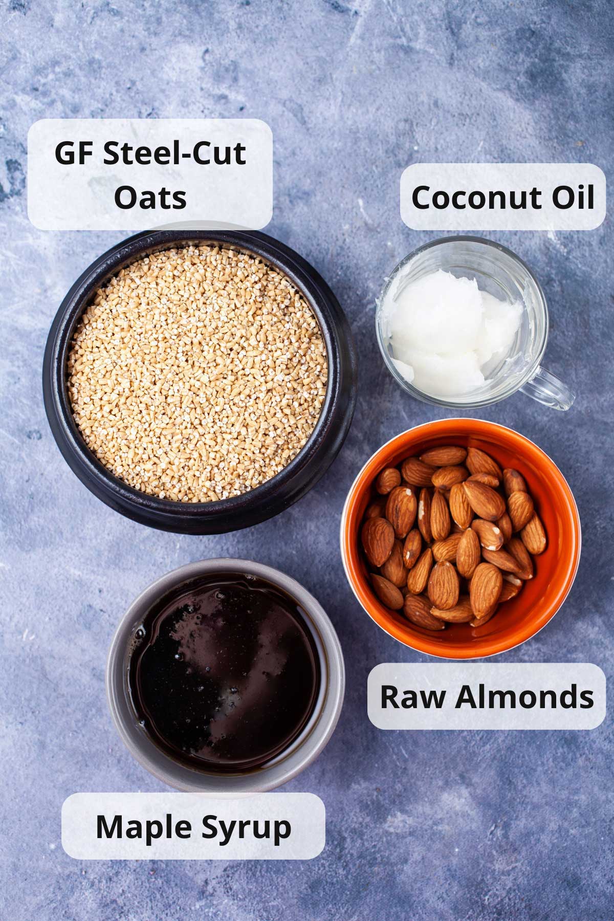 Gluten-free steel cut oats, coconut oil, maple syrup, and raw almonds displayed on a table.