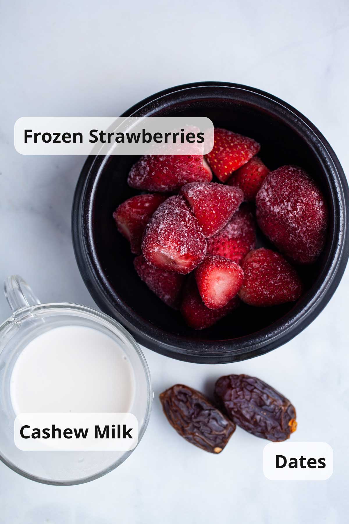 Frozen strawberries, cashew milk, and dates on a table.