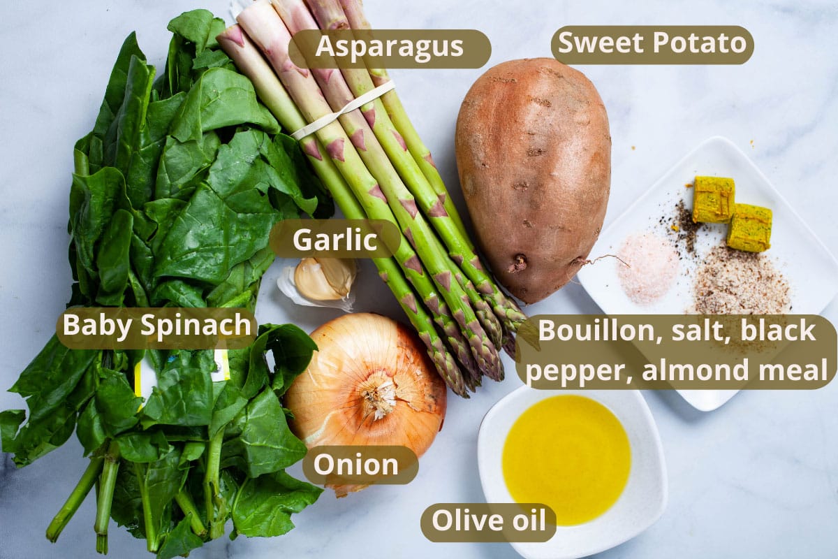 Asparagus, one sweet potato, garlic, baby spinach, one onion, olive oil, one bouillon, salt, black pepper, and almond meal displayed on a table.