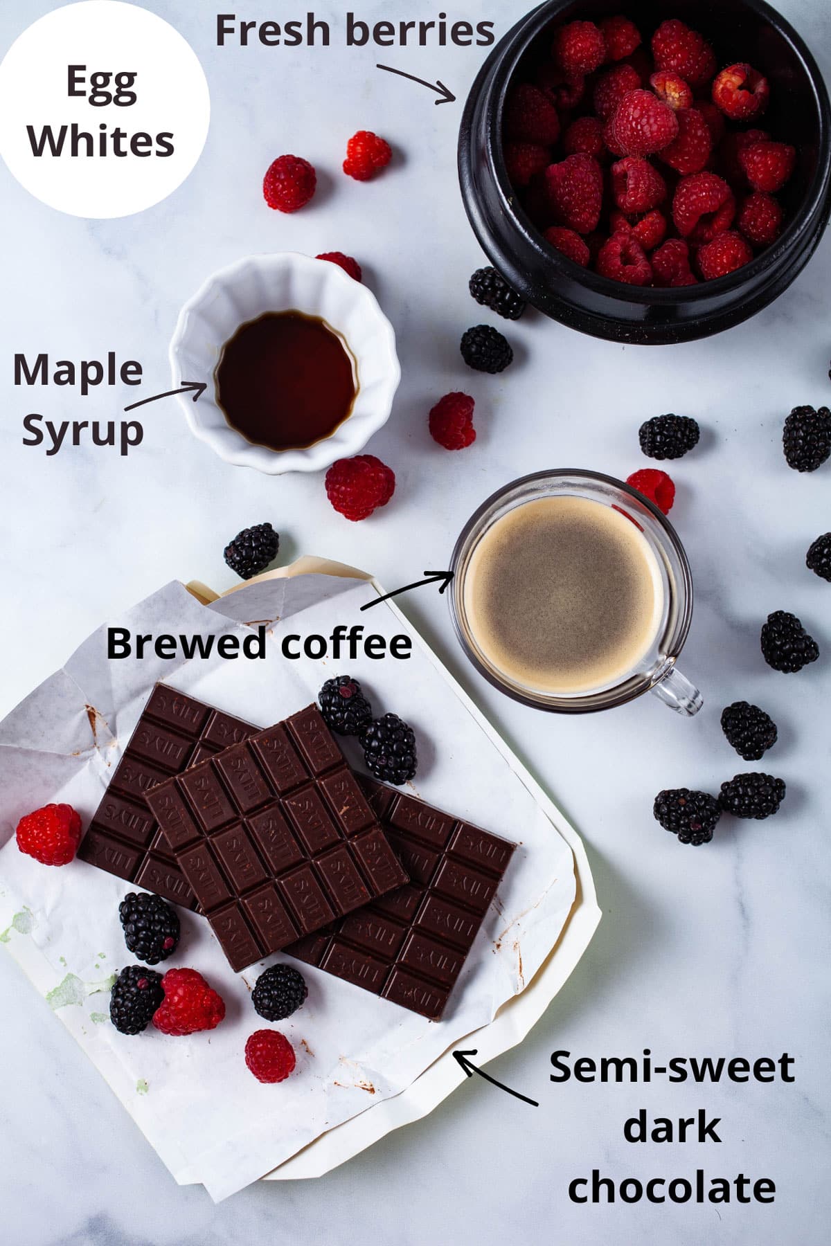 Ingredients such as egg whites, fresh berries, maple syrup, brewed coffee, and semi-sweet dark chocolate laid out on a white background.