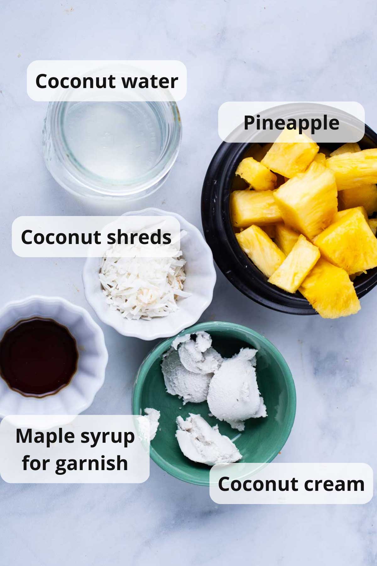 Fresh pineapple, coconut cream, coconut water, fine coconut shreds, and maple syrup displayed on a table.