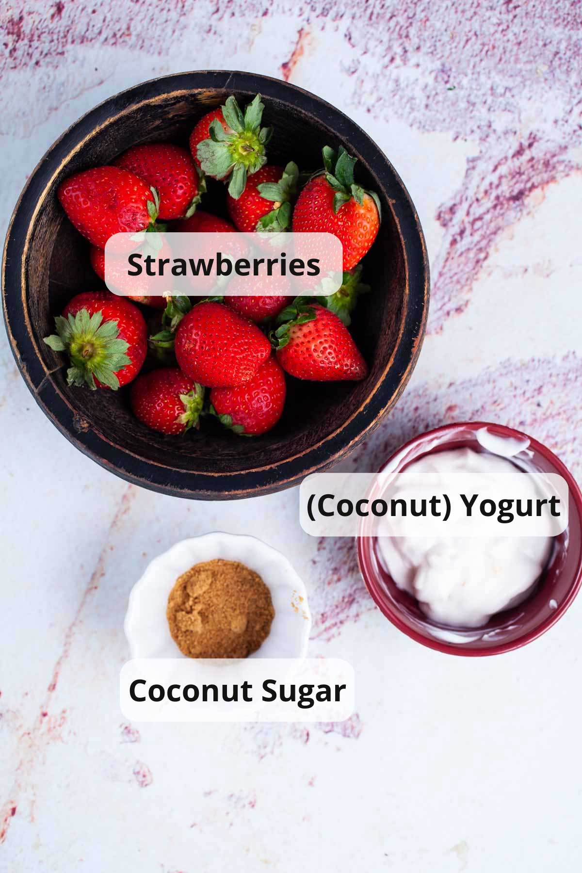 Fresh strawberries, coconut yogurt, and coconut sugar displayed on a table.