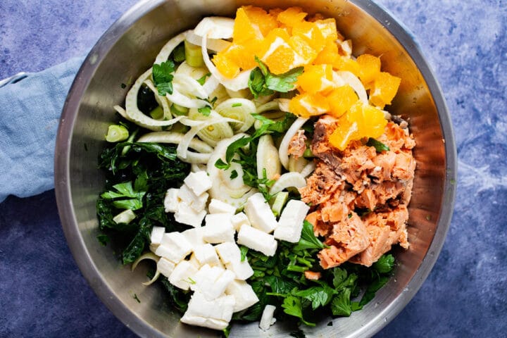 A bowl filled with raw chopped green kale, canned salmon, fennel, oranges, parsley, and mozzarella cheese.