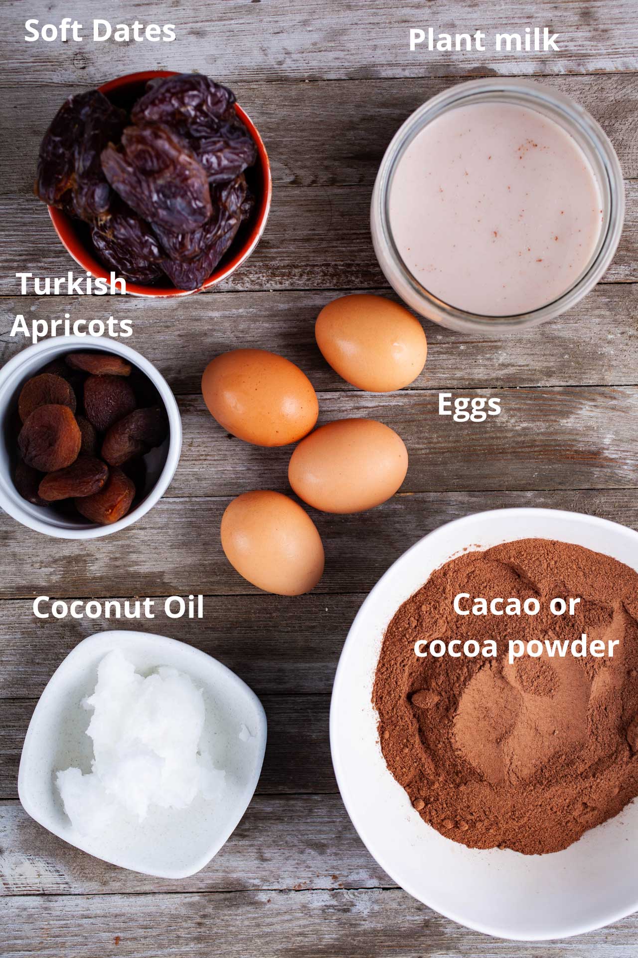 Soft dates, plant milk, Turkish apricots, eggs, coconut oil, and cacao or cocoa powder displayed on a wooden board.