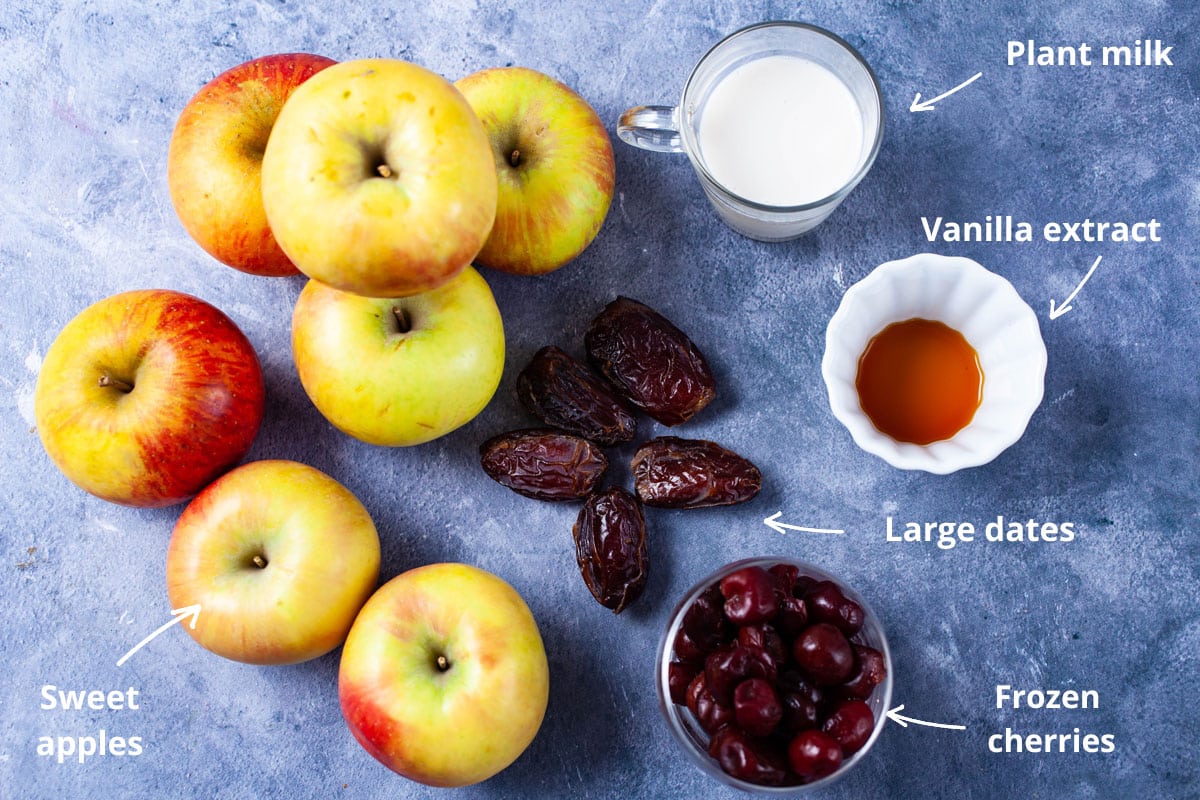 Plant milk, vanilla extract, large dates, frozen cherries, sweet apples on a table.