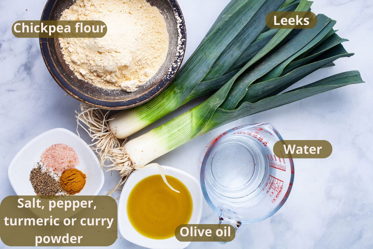 Chickpea flour, leeks, water, salt, pepper, curry powder, and olive oil displayed on a table.