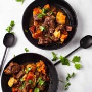 Two black plates filled with a hearty potato and beef stew.