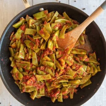 Italian green beans in a pan coated with tomato sauce.